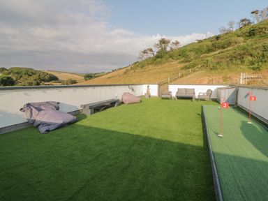 An outdoor rooftop area with artificial grass seating a putting green and a bench at 12 Beachdown in Challaborough