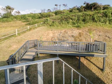 An outdoor wooden deck with railing and stairs on a hillside with plants at 12 Beachdown in Challaborough