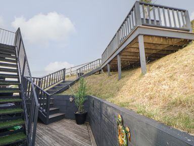 An outdoor area with wooden stairs, a deck, grass slope, and a potted plant at 12 Beachdown in Challaborough