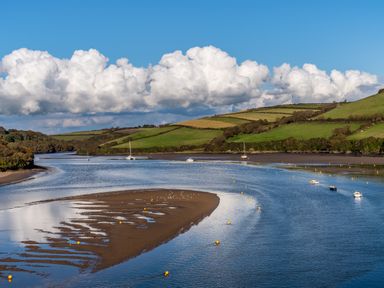 A river with boats and green hills under a blue sky with clouds at 12 Beachdown in Challaborough