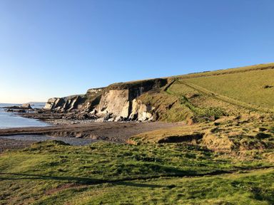 A coastal landscape with cliffs grassy hills and a rocky shoreline at 12 Beachdown in Challaborough