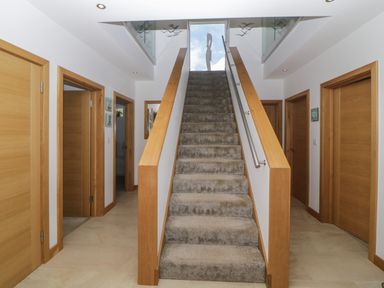 A carpeted staircase with wooden railings in a hallway with multiple wooden doors at 12 Beachdown in Challaborough
