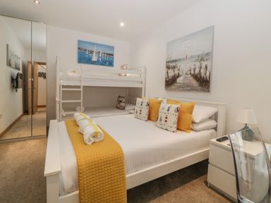 A bedroom with a double bed and bunk bed with yellow and patterned pillows and wall art at 12 Beachdown in Challaborough