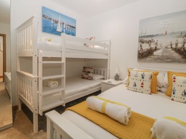 A bedroom with a white bunk bed a double bed with pillows and towels and paintings on the walls at 12 Beachdown in Challaborough