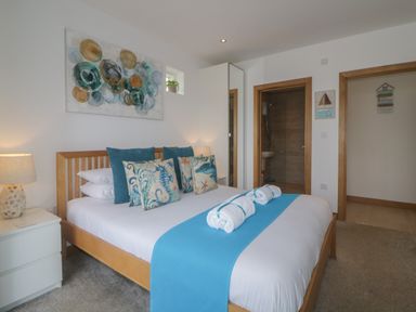 A bedroom with a wooden bed frame blue and sea-themed cushions a blue runner on the bed and bedside tables at 12 Beachdown in Challaborough