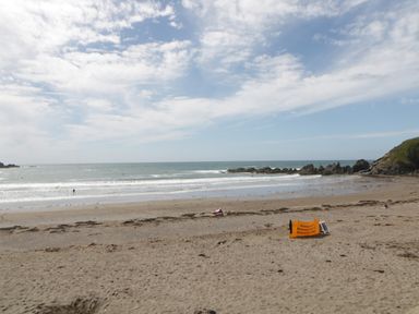 A sandy beach with scattered seaweed and a safety sign near the shoreline and waves at 12 Beachdown in Challaborough