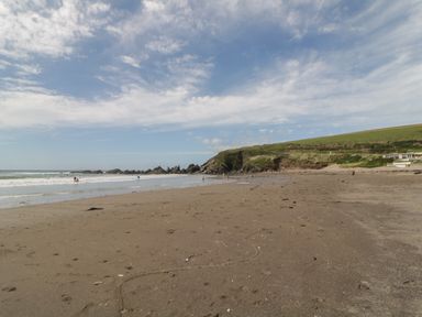 A sandy beach with people near the water and rocky cliffs in the background at 12 Beachdown in Challaborough
