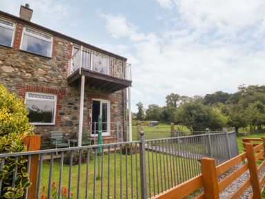A stone house with a small balcony and garden area enclosed by metal and wooden fences at Coed y Glyn Bach Equestrian in Penygroes