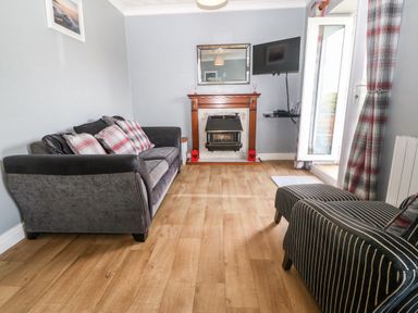 A living room with a sofa armchair fireplace wall mounted tv and open door with curtains at Coed y Glyn Bach Equestrian in Penygroes