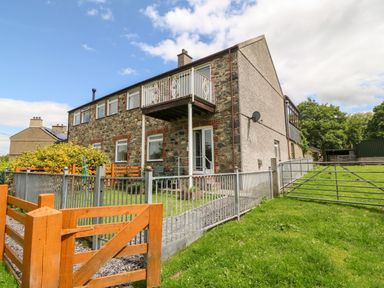 A stone and brick house with a balcony and fenced yard at Coed y Glyn Bach Equestrian in Penygroes