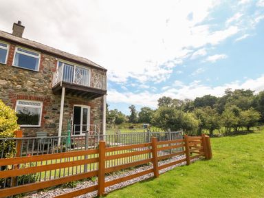 A stone house with a balcony and fenced garden adjacent to a grassy field with trees at Coed y Glyn Bach Equestrian in Penygroes