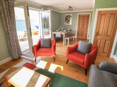 A sitting area with two orange armchairs and a gray sofa near glass doors leading outside at The Annexe Meadow Croft in Haverfordwest