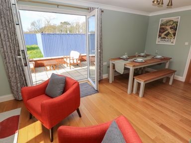 A dining room with table set for four and red chairs next to an open door leading to a patio at The Annexe Meadow Croft in Haverfordwest