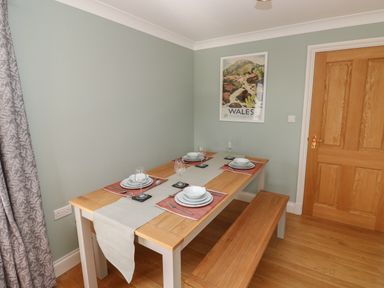 A dining room with a wooden table set for four and a Wales poster on the wall at The Annexe Meadow Croft in Haverfordwest