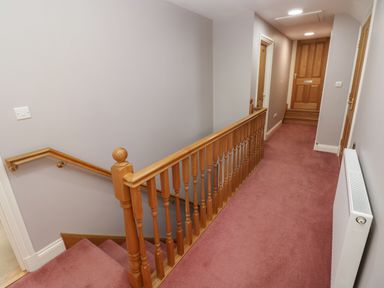 A hallway with carpet stairs wooden railing radiator and wooden doors at The Annexe Meadow Croft in Haverfordwest