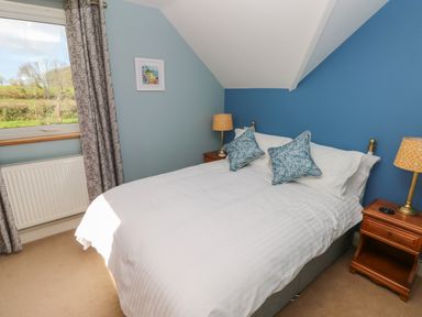 A bedroom with a double bed pillows bedside tables lamps window with curtains and a radiator at The Annexe Meadow Croft in Haverfordwest