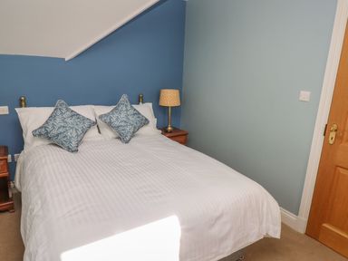 A bedroom with a bed white bedding two blue patterned cushions wooden bedside tables and a lamp at The Annexe Meadow Croft in Haverfordwest
