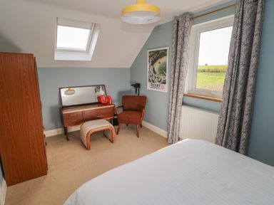 A bedroom with a bed a wooden wardrobe a dressing table with a mirror a chair an ottoman and a window with curtains at The Annexe Meadow Croft in Haverfordwest