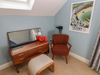 A dressing table with a mirror and lamp next to a chair and a stool in a room with a blue wall at The Annexe Meadow Croft in Haverfordwest