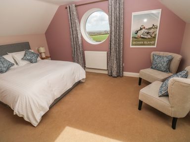 A bedroom with a bed a bedside table two armchairs a round window and a framed picture at The Annexe Meadow Croft in Haverfordwest