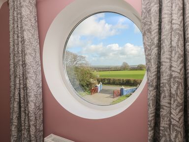A round window with curtains showing a view of a green field and a gate at The Annexe Meadow Croft in Haverfordwest