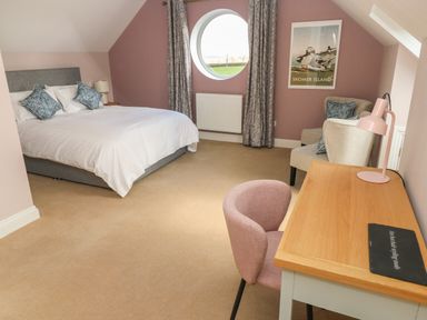 A bedroom with a double bed pillows armchairs a desk and a circular window at The Annexe Meadow Croft in Haverfordwest