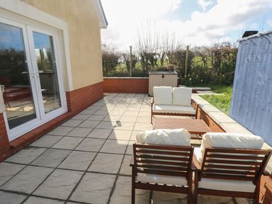 An outdoor patio with tiled floor wooden chairs with cushions and a wooden table at The Annexe Meadow Croft in Haverfordwest