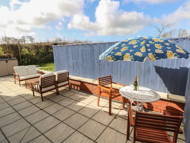 A patio with wooden chairs a small table with an umbrella and a seating area with cushions at The Annexe Meadow Croft in Haverfordwest