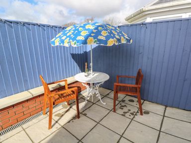 A small outdoor patio with two wooden chairs a white metal table with a floral umbrella and a bottle on the table at The Annexe Meadow Croft in Haverfordwest