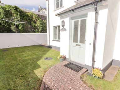 An exterior view of a house entrance with a green door and a brick path surrounded by grass at 3 Strawberry Close in Little Haven near Broad Haven