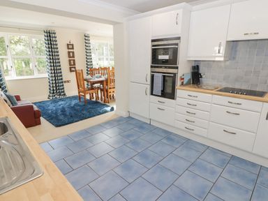 A kitchen with white cabinets and blue tiled floor opening into a dining area with wooden table and chairs at 3 Strawberry Close Little Haven near Broad Haven