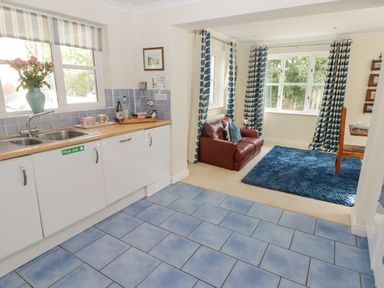 A kitchen with blue tiled floor and white cabinets next to a sitting area with a red sofa and blue patterned curtains at 3 Strawberry Close in Little Haven near Broad Haven