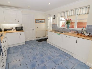 A kitchen with blue tiled floor white cabinets wooden countertops and a window with striped blinds at 3 Strawberry Close in Little Haven near Broad Haven