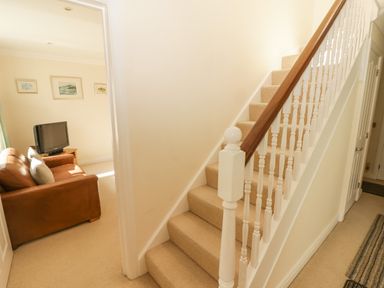 A carpeted staircase with wooden handrail next to a living room with a brown leather sofa and a television at 3 Strawberry Close in Little Haven near Broad Haven