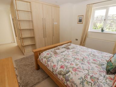 A bedroom with a wooden bed with floral bedding and rolled towels near a window and a large wardrobe at 3 Strawberry Close in Little Haven near Broad Haven