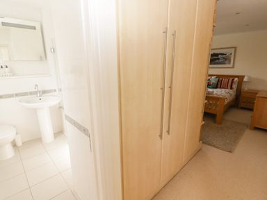 A hallway with wooden wardrobes leading to a bedroom and a bathroom with a sink and toilet at 3 Strawberry Close in Little Haven near Broad Haven
