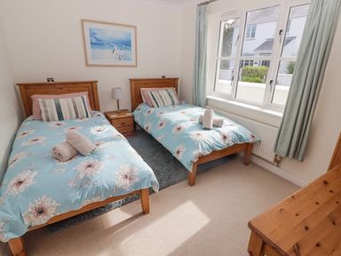 A bedroom with two single beds blue floral bedding side table lamp and window with curtains at 3 Strawberry Close in Little Haven near Broad Haven