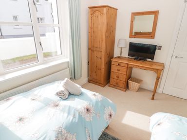 A bedroom with a bed with floral bedding a wooden wardrobe wooden desk with a lamp and TV and a mirror on the wall at 3 Strawberry Close Little Haven near Broad Haven