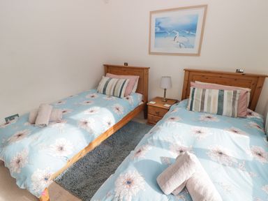 A bedroom with two single wooden beds blue floral bedding a nightstand with lamp and framed picture at 3 Strawberry Close Little Haven near Broad Haven