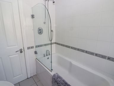 A bathroom with a white bathtub and glass shower screen at 3 Strawberry Close in Little Haven near Broad Haven