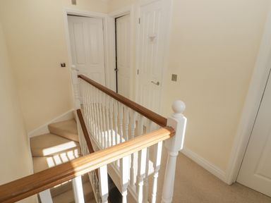 A hallway with a staircase and three closed doors at 3 Strawberry Close in Little Haven near Broad Haven