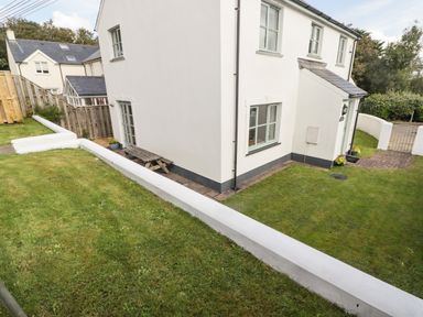 The exterior of a white house with grass lawn and a wooden picnic table at 3 Strawberry Close in Little Haven near Broad Haven