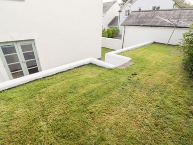 A lawn area with white walls surrounding a building with glass double doors at 3 Strawberry Close in Little Haven near Broad Haven