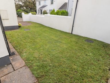 A small grass yard with a white wall and a gate outside a white house at 3 Strawberry Close in Little Haven near Broad Haven
