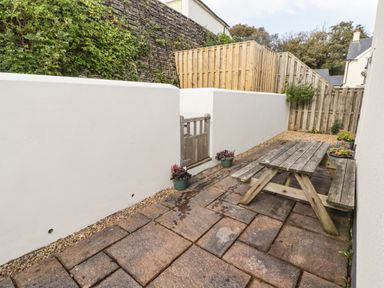 An outdoor patio area with a wooden picnic table potted plants stone paving and a wooden gate at 3 Strawberry Close in Little Haven near Broad Haven