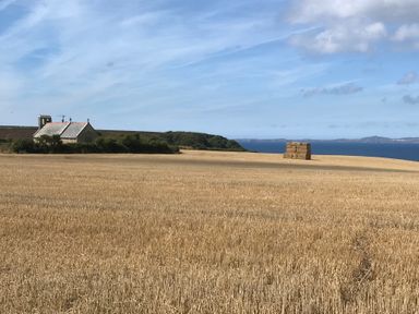 A field with cut hay bales near a small stone church by the sea at 3 Strawberry Close in Little Haven near Broad Haven