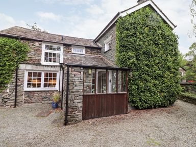Exterior view of a stone house with white framed windows and a porch covered in glass at Holly Cottage in Grasmere