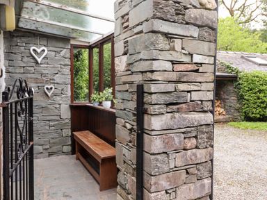 A stone entrance area with a wooden bench plants on a window ledge and heart decorations on the wall at Holly Cottage in Grasmere