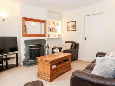 A living room with leather sofas a wooden coffee table a TV a stone fireplace and a bookshelf at Holly Cottage in Grasmere