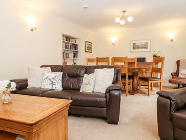 A living room with brown leather sofas wooden coffee and dining table chairs and bookshelves at Holly Cottage in Grasmere